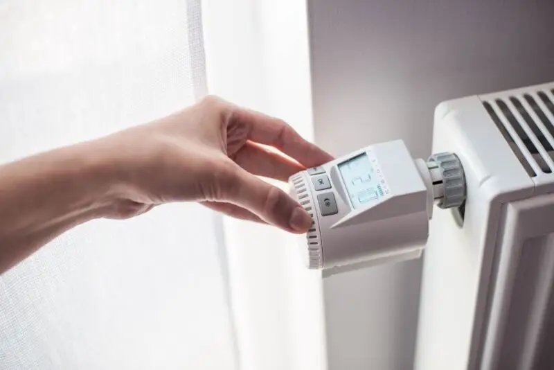 Osoba reguluje temperaturę za pomocą termostatu grzejnika elektrycznego